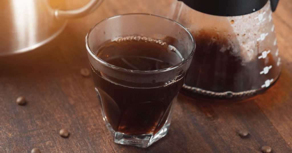 glass of coffee next to a glass carafe