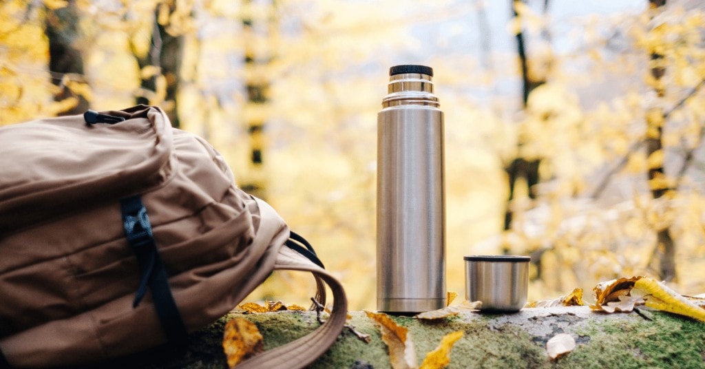 coffee thermos in nature next to a backpack