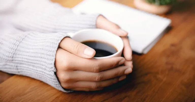 hands holding a cup of black coffee
