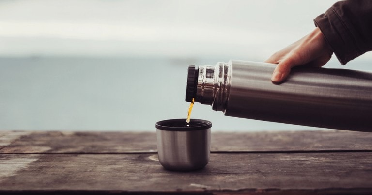 person pouring coffee out of a thermos into the lid cup
