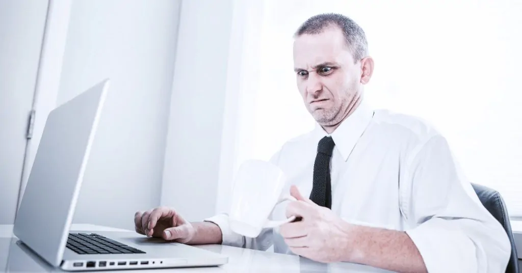 man at an office desk looking into a cup of coffee disgustedly