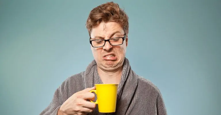 man looking down at his coffee mug making a grimace