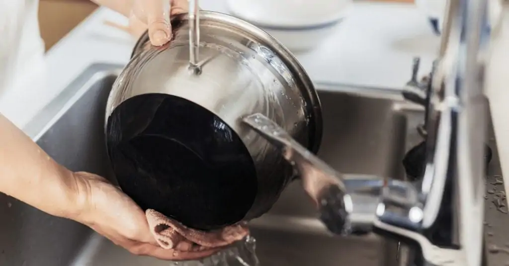 person washing a metal cooking pot