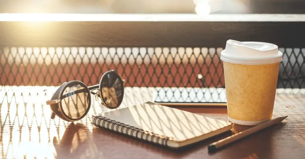 to go coffee cup next to a notebook and sunglasses