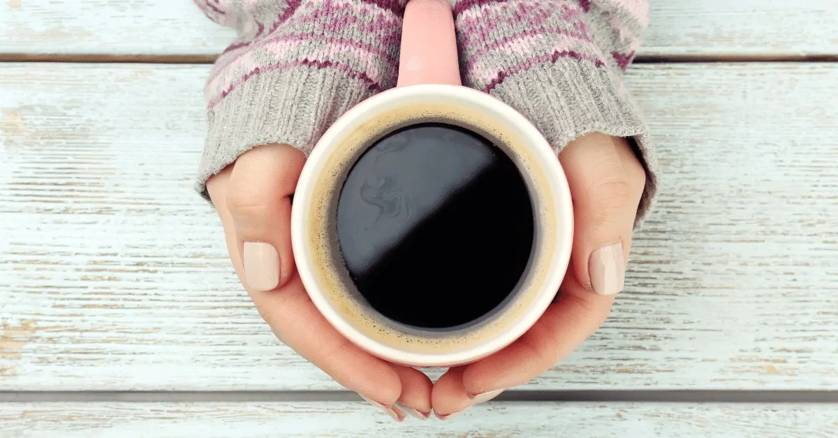hands holding a mug of black coffee