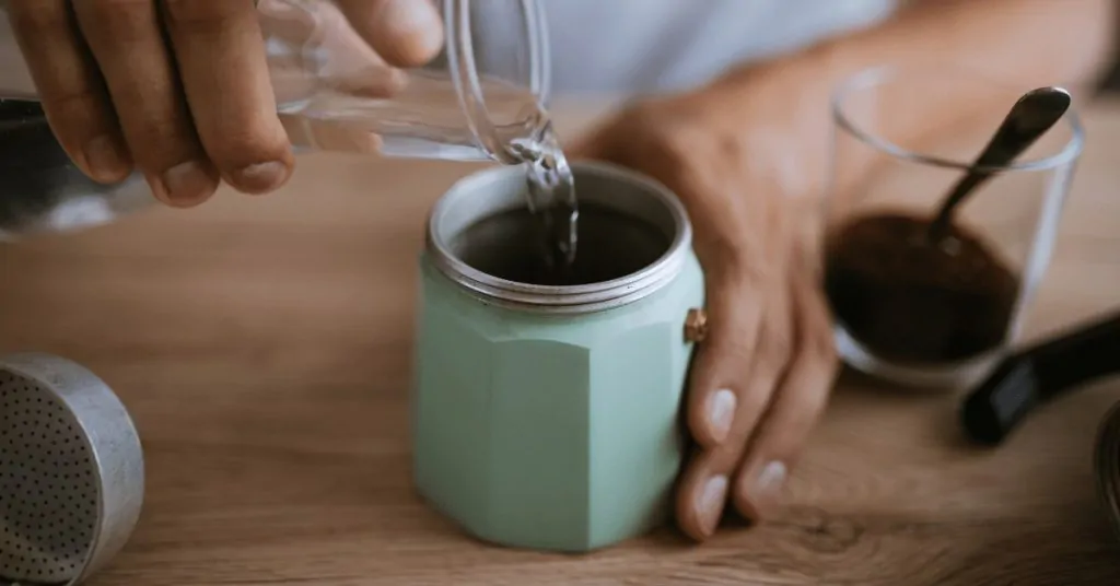 person pouring water into the bottom of a mint green moka pot