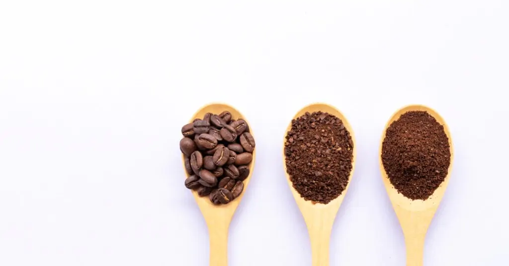 whole coarse and finely ground coffee beans on wooden spoons