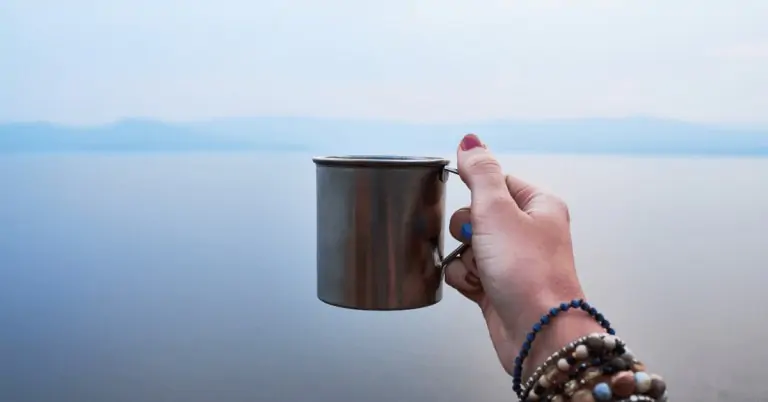 woman holding a metal mug by a lake