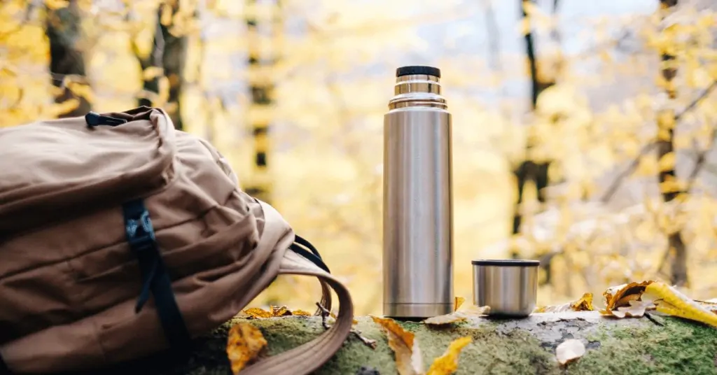 coffee thermos in nature next to a backpack