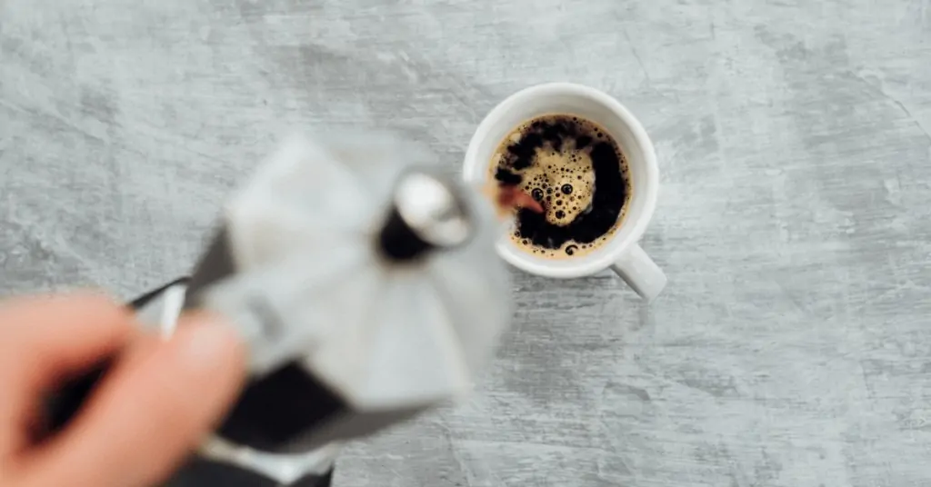 person pouring coffee from a moka pot into a cup