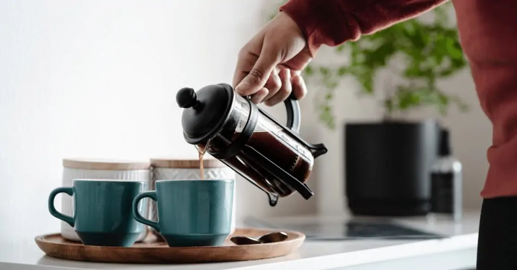 person pouring coffee out of a french press into coffee cups