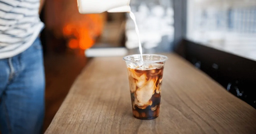 person pouring milk into a cup of cold brew coffee
