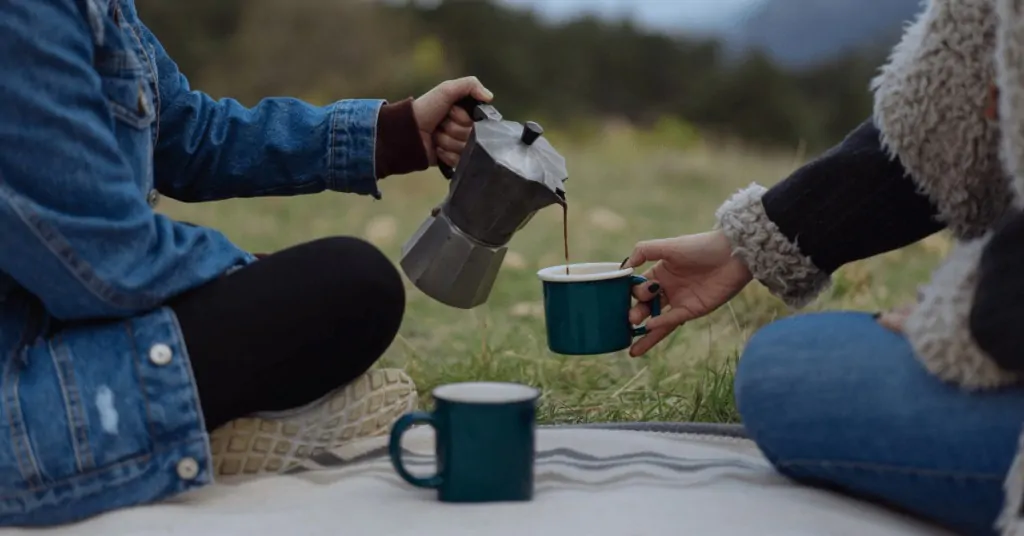 woman pouring coffee from a moka pot into the cup of another woman