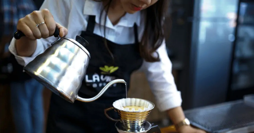 woman pouring water out of a gooserneck kettle into a kalita wave brewer