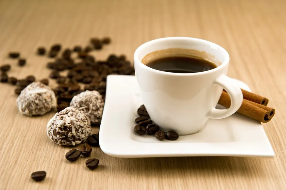 Cup of coffee with beans and truffles over wooden background